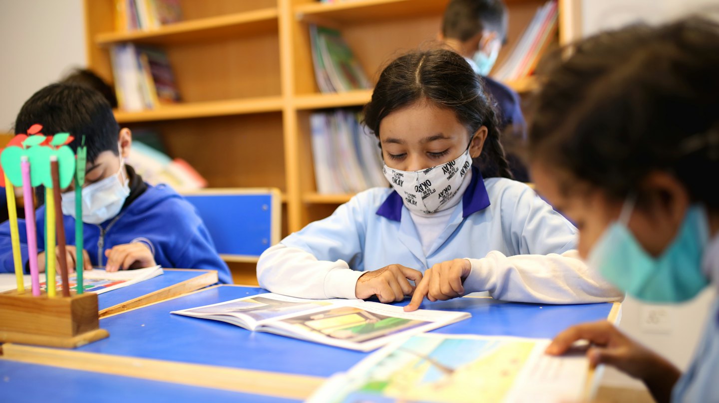 Tres estudiantes estudian juntos en una mesa azul en una biblioteca.