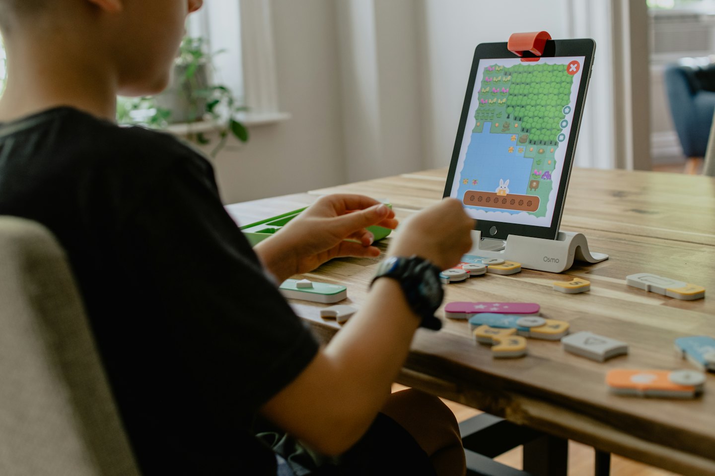 Niño juega juego educativo en tablet con piezas físicas.