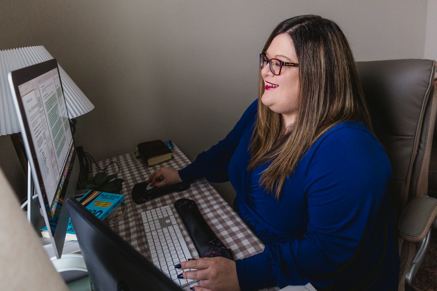 Mujer sonriendo mientras trabaja en una computadora en un escritorio de oficina en casa.